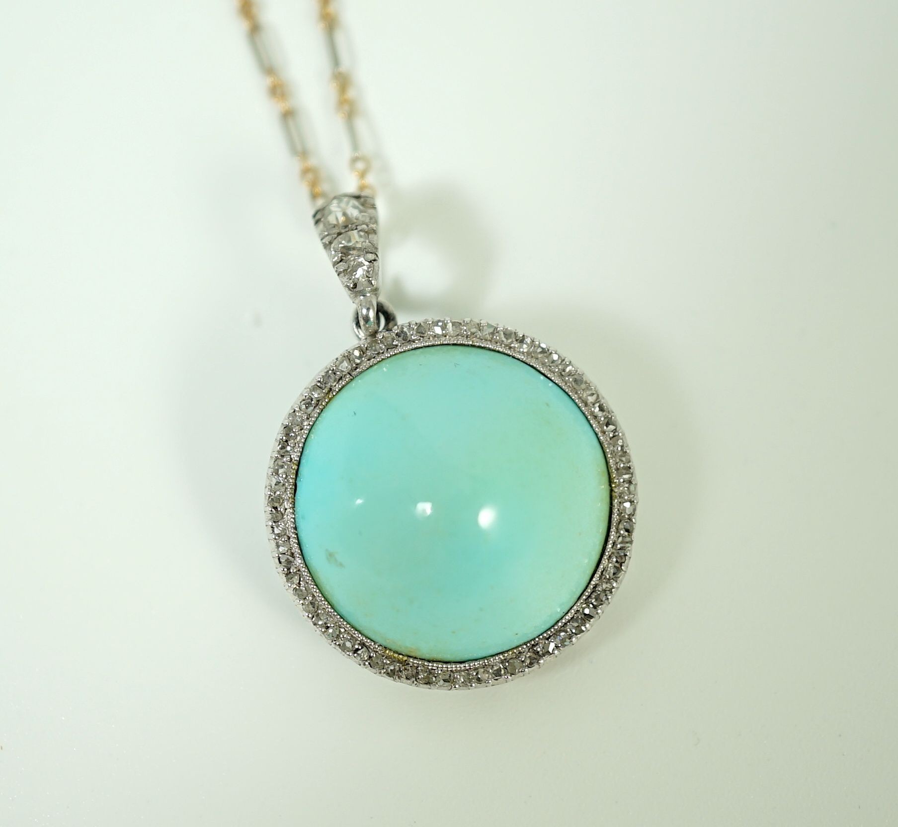 An early 20th century platinum and turquoise set pendant, with diamond chip border and diamond set bale, on a 15ct two colour gold fine link chain